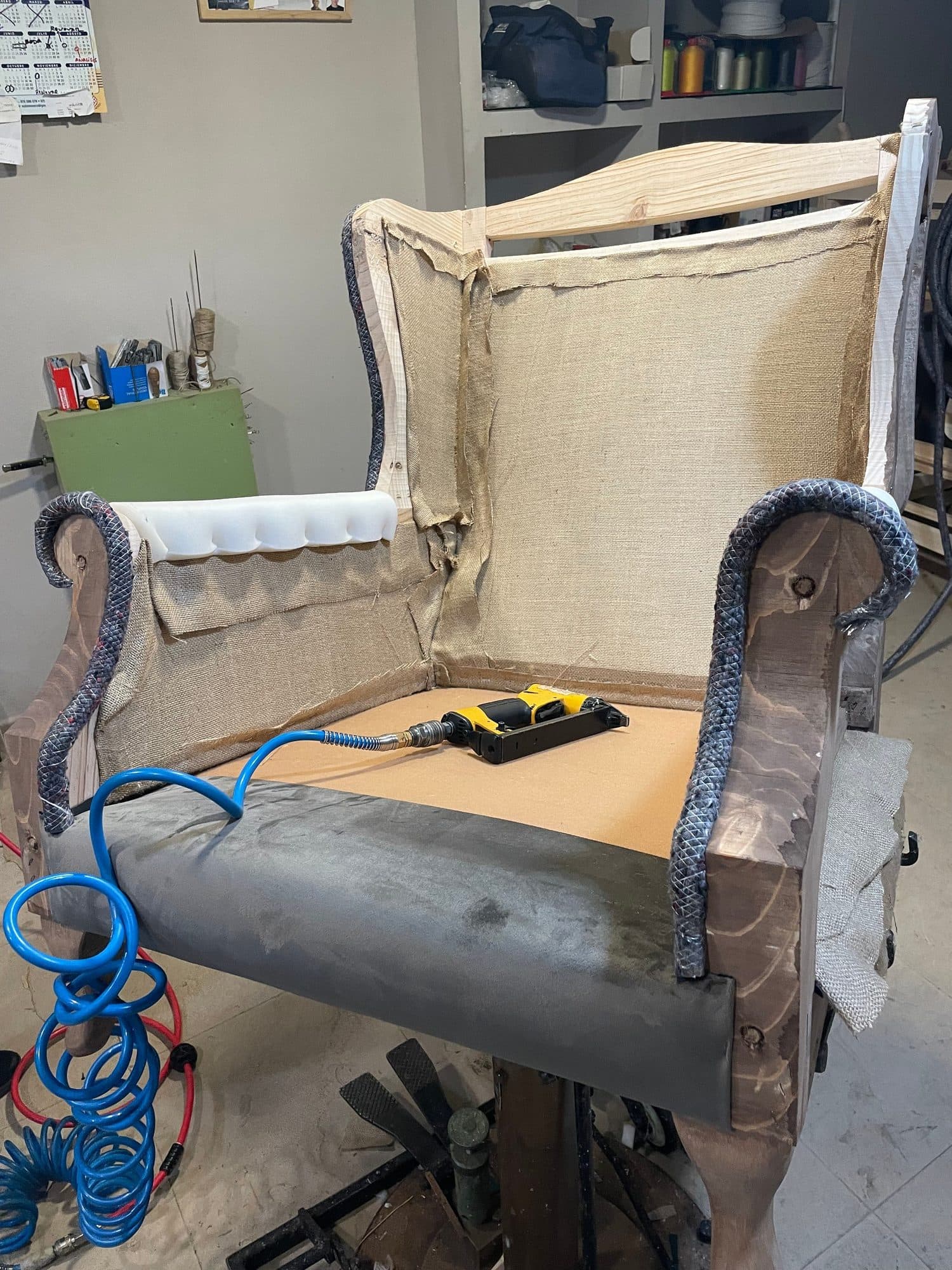 Sillón orejero en proceso de tapizado sobre el caballete del taller